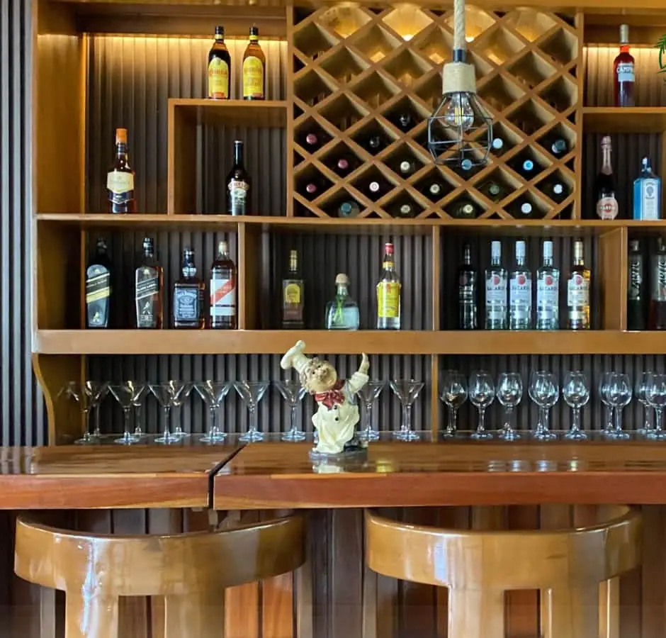 The bar: timber shelves of bottles and glasses above a counter with stools.