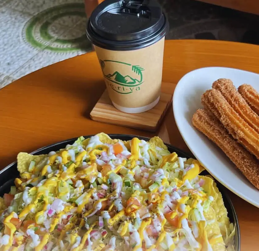 A Seriva coffee cup beside a plate of churros and a platter of nachos.