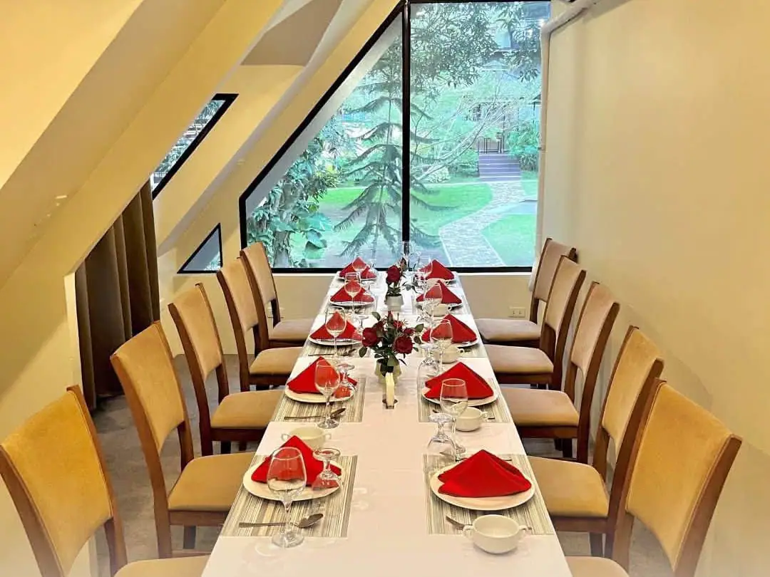 A long table set with red napkins for private dining, beside a tall window onto the garden.