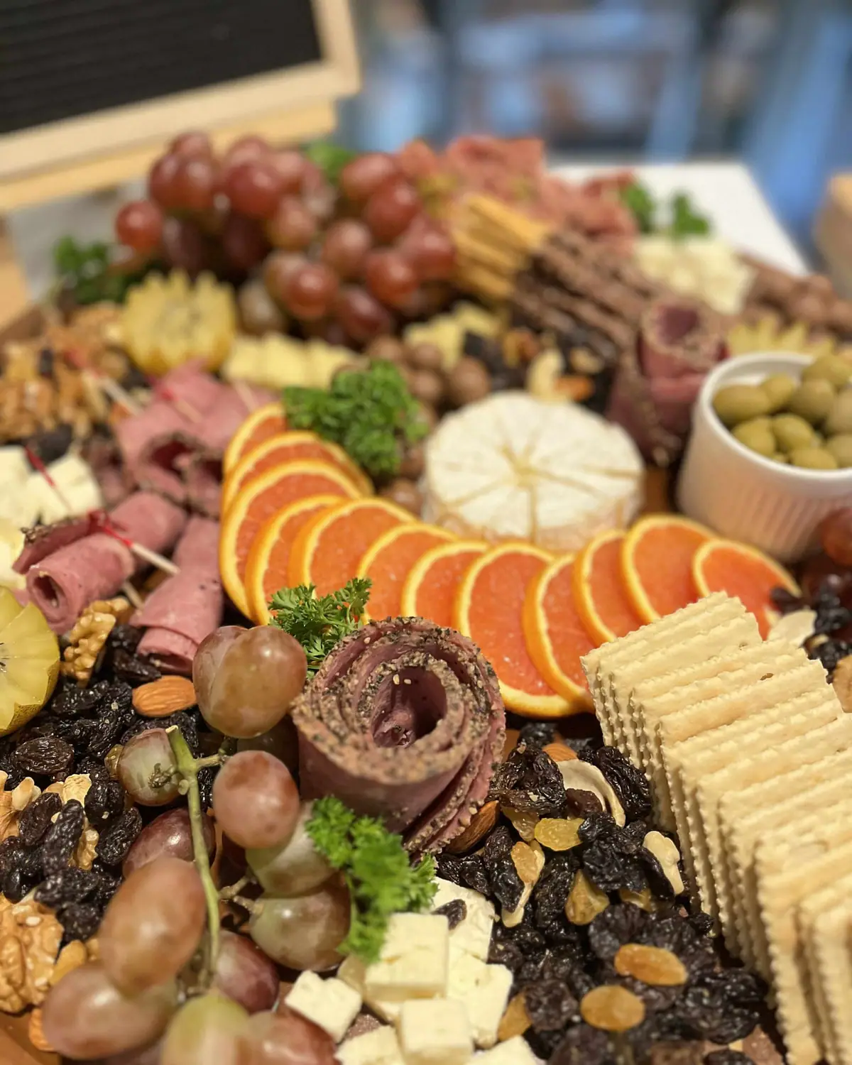 A charcuterie board of grapes, cured meats, cheese, oranges and crackers.