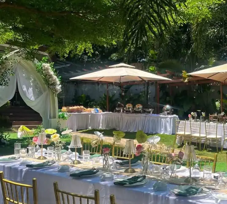 Tables, umbrellas and a flower arch set up on the lawn for a garden event.