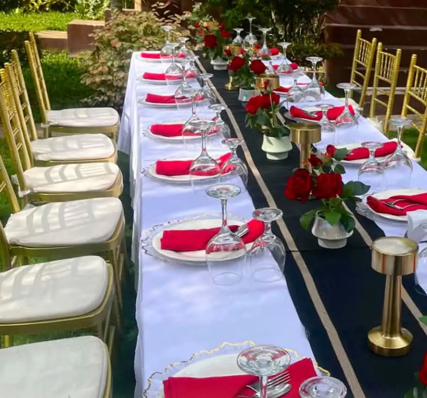 A long table set for an event, with red roses, red napkins and gold chairs.