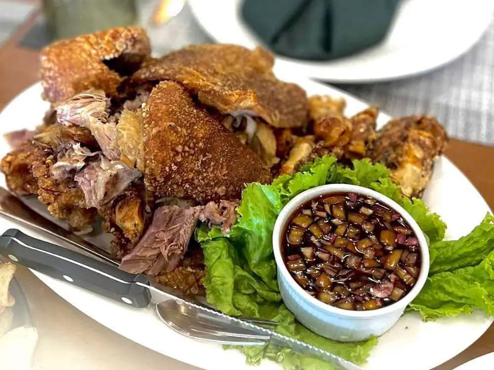 Crispy pata on a plate with lettuce and a bowl of dipping sauce.