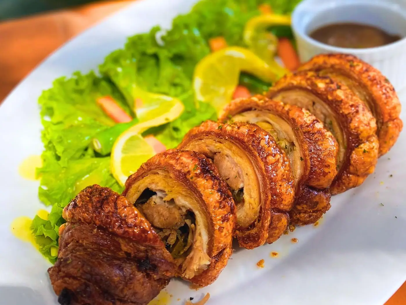 Sliced porchetta with salad, lemon and a cup of gravy.