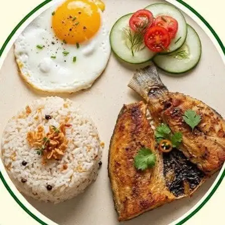 Fried milkfish with a fried egg, garlic rice, cucumber and tomato.